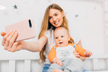 mother and a small baby relax while sitting on the bed and take a selfie on their mobile phone.