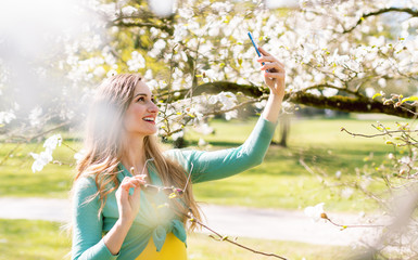 Young woman taking selfie with her phone in park at tree blossom