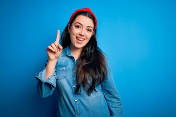 Young brunette woman wearing casual denim shirt over blue isolated background pointing finger up with successful idea. Exited and happy. Number one.