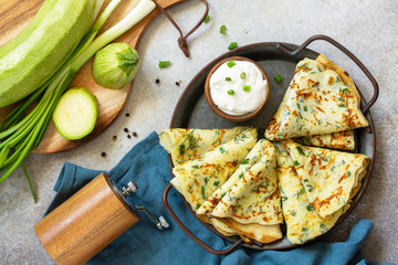 Snack or summer lunch. Zucchini pancakes with herbs served with sour cream in a plate on a gray...