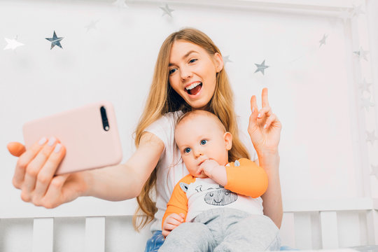mother and a small baby relax while sitting on the bed and take a selfie on their mobile phone.