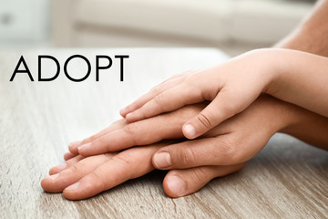 Happy family holding hands at wooden table indoors, closeup. Child adoption concept