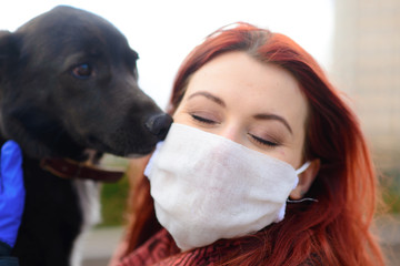 Young female using a face mask as a coronavirus spreading prevention walking with her dog. Global...