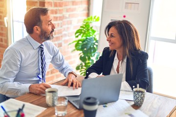 Two middle age business workers smiling happy and confident. Working together with smile on face using laptop at the office