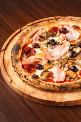 Pontremolina. Hot Italian pizza with Piennolo tomatoes, turkey ham, artichokes, oregano and salami. Original recipe. Pizza on wooden background