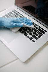 The woman cleans the keyboard of her computer to protect it from coronavirus. She uses the cleaning cloth and mitt.