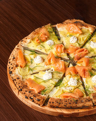 Original Italian seafood pizza. Original recipe. Cutted pizza with potato, smoked salmon, cream and leaves on wooden table. True and authentic.