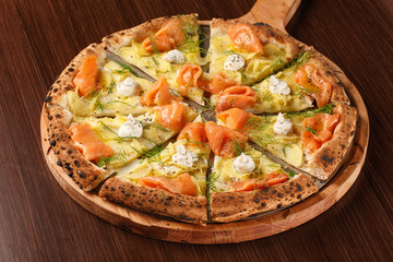 Original Italian seafood pizza. Original recipe. Cutted pizza with potato, smoked salmon, cream and leaves on wooden table. True and authentic.