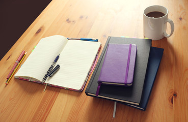 tidy workspace background to study or work at home - open blank notebook with pens, books and a cup of coffee on a wooden table of a freelance office