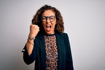 Middle age brunette business woman wearing glasses standing over isolated white background angry and mad raising fist frustrated and furious while shouting with anger. Rage and aggressive concept.