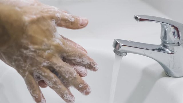 Slow motion, 120 fps, close up. A man is washing his hands to avoid getting infected by the widespread corona virus. Unrecognizable person thoroughly washes their hands with antibacterial soap. 