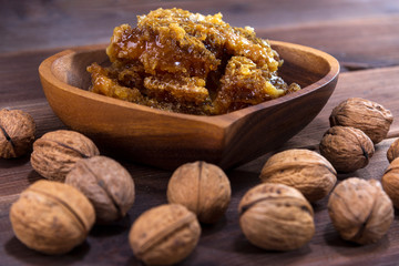 Honeycombs with honey in a wooden plate and many inshell walnuts on a wooden surface