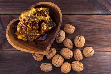 Honeycombs with honey in a wooden plate and many inshell walnuts on a wooden surface. View from above