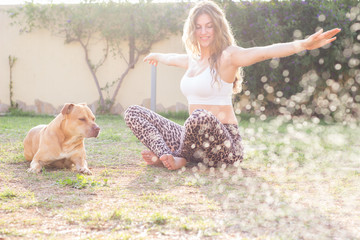 Young beautiful woman practicing yoga with her dog outdoors - 341073829