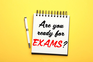 Stylish notebook with phrase ARE YOU READY FOR EXAMS and pen on yellow background, top view