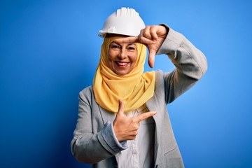 Middle age brunette architect woman wearing muslim traditional hijab and security helmet smiling making frame with hands and fingers with happy face. Creativity and photography concept.