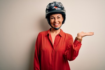 Middle age motorcyclist woman wearing motorcycle helmet over isolated white background smiling cheerful presenting and pointing with palm of hand looking at the camera.
