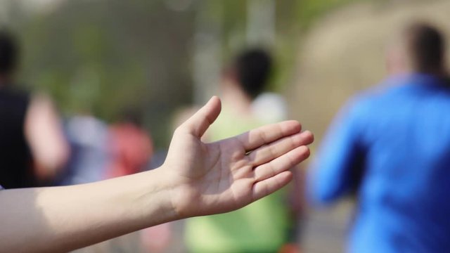 Shot unrecognizable runners on city street for commercial use. Spectator claps and gives five marathon participants running under bright sunshine closeup. Unrecognizable runners on city street