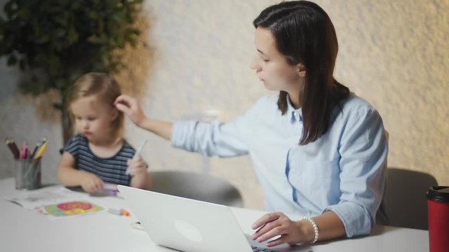 Young mother working on laptop while her child painting near to her