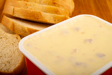 Sliced loaf of wheat bread and melted cheese in a plastic tray on a wooden cutting Board. Close up.