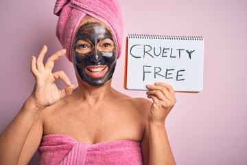 Middle age brunette woman wearing cruelty free beauty black face mask doing ok sign with fingers,...
