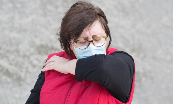 Woman on the street cough up in protective mask,having Covid-19 symptom.Female with safety protection wear in the city during Corona virus coughing in her elbow for protection spreading virus microbes - Powered by Adobe