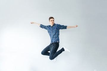 Fototapeta na wymiar Young man in a blue shirt and black trousers jumps on a light gray background