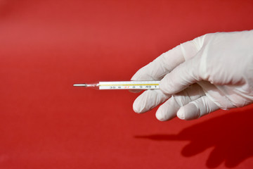Hand in white medical glove holds medical mercury thermometer.Defocused photo.