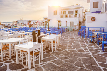 Picturesque narrow street with traditional whitewashed houses with cafe tables of Naousa town in famous tourist attraction Paros island, Greece on sunrise