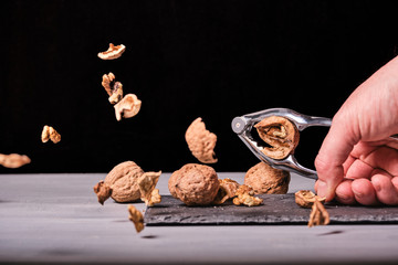 Man cracking nuts with a nutcracker over a slate and a  grey wood. Black background. Nutshells in the air.