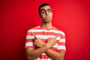 Young handsome african american man wearing casual striped t-shirt and glasses Pointing to both sides with fingers, different direction disagree