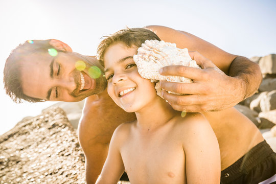 Father and son having fun on the beach and listening to the ocean in a shell