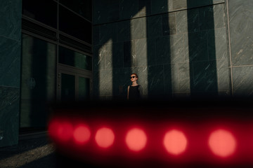 Elegant woman wearing sunglasses, leaning on wall with shadows and red lights