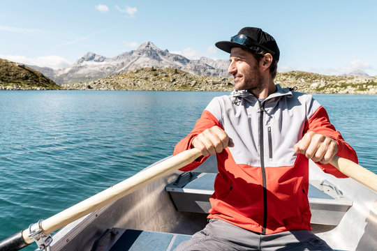 Young smiling man in a rowing boat, Lake Suretta, Graubuenden, Switzerland