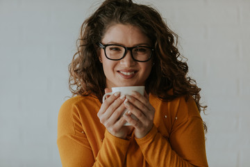 Portrait of attractive young woman with curly hair enjoying her coffee. Smiling young woman is posing in front of camera.
