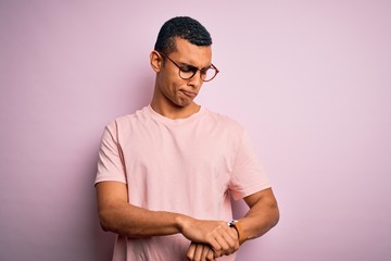 Handsome african american man wearing casual t-shirt and glasses over pink background Checking the time on wrist watch, relaxed and confident