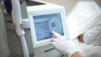 Young female doctor wearing gloves at beauty clinic cosmetology service setting up laser system touching display of device close-up
