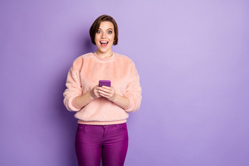 Fototapeta na wymiar Photo of funny blogger lady open mouth holding telephone hands read interesting creative idea wear casual stylish pink pullover trousers isolated purple color background
