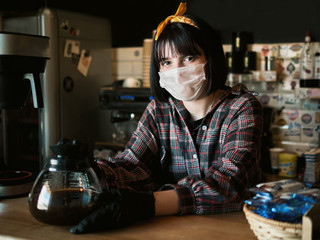 Concept of biohazard security and social responsibility in coronavirus epidemic measures to contain virus spread: young barista girl in medical mask and medical gloves holding coffee jug in city cafe