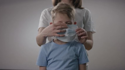 Mother in white tee is putting on a medical mask on her child in order to prevent him from being infected by Covid19