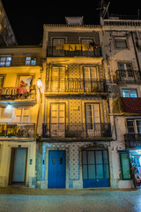 old house with balconies and a blue door, illuminated by a yellow lantern on a night street