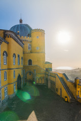 the courtyard of the yellow castle with an arched entrance with a staircase and a dome of the tower against the backdrop of hills, sea and sunset