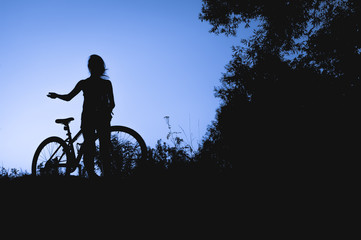 silhouette of a young girl with a bicycle at sunset in the middle of nature