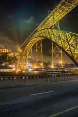 road and old metal arch bridge in the rays of spotlights against the night sky and luminous houses