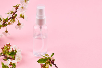 bottle with transparent liquid. alcohol hand sanitizer over pink background with flower decoration.