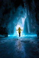 a girl in a yellow jacket stands at the exit of an ice cave in bright light