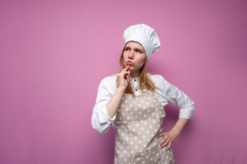 thoughtful beautiful girl cook in kitchen clothes thinks over an idea on a pink background, a woman housewife dreams and looks at a place for text