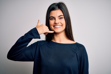 Young beautiful brunette woman wearing casual sweater standing over white background smiling doing phone gesture with hand and fingers like talking on the telephone. Communicating concepts.