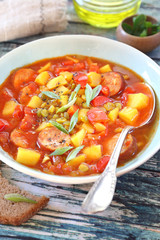 Spicy pea soup with potatoes, tomatoes, sausages and slices of bread