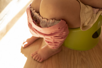 Peeing or pooping baby on a green pot. Weaning from a diaper. Pink polka-dot leggings and baby...